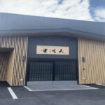 施設の玄関入口。木調の建物外壁に施設名の看板が掲げられている